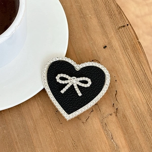 Macro shot of heart-shaped black leather phone grip with sparkling rhinestone bow detail