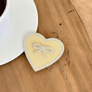 Detail of heart-shaped phone grip with cream lychee leather and crystal bow on wood