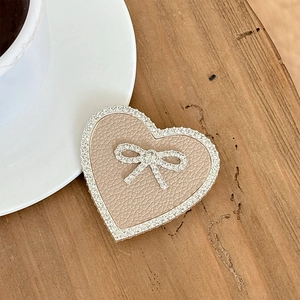 Macro detail of heart-shaped phone grip with rhinestones and bow on wooden background