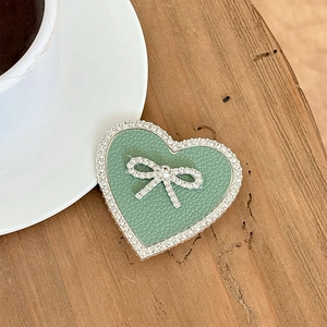 Close-up of mint green leather heart phone grip with rhinestone bow on wooden table