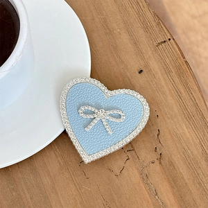 Blue heart-shaped leather phone grip with crystal bow decoration on a wooden desk