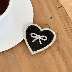 Detail of heart-shaped phone grip with black leather texture and rhinestone bow on wood