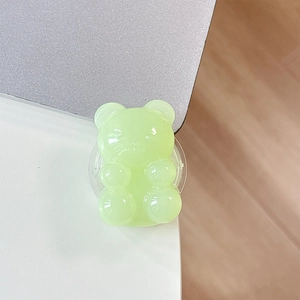 Close-up of translucent jelly green bear phone grip on a white desk workspace