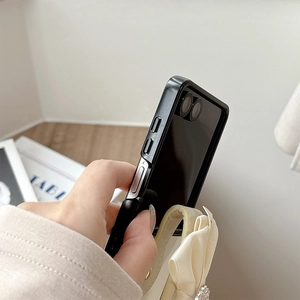 Close-up of black mirror phone case featuring a cream silk bow strap and metal side buttons