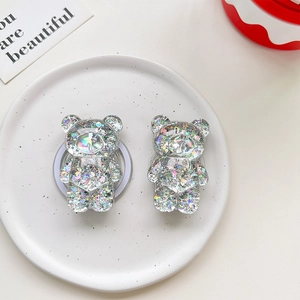 Macro detail of 3D bear-shaped glitter phone grips on a stylish ceramic display tray
