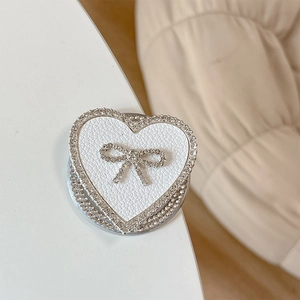 Macro shot of heart-shaped phone grip with white lychee leather and rhinestone bow detail