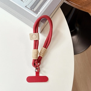 Close-up of red braided phone wrist strap with leather smile charm on white table