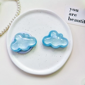 Detail view of cloud-shaped glitter phone grips in pearlescent blue on a ceramic plate