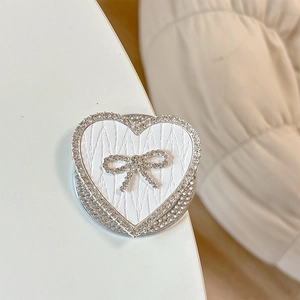 Macro detail of heart-shaped phone grip with rhinestone bow and wave-textured surface