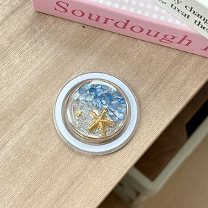 Detail of a round ocean-themed phone grip with starfish, seashells and blue shell stones