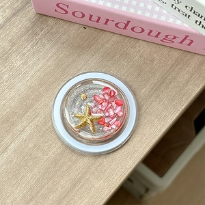 Detail of a phone grip with pink shells and gold starfish on a light wood background