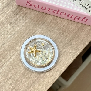 Close-up of ocean-themed phone grip featuring a gold starfish and shell inside clear resin