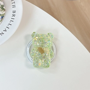 Détail du support téléphone ours vert avec paillettes et design de cœur sur socle blanc