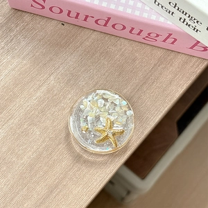 Detail of a round seashell phone grip with a gold starfish and resin ocean design