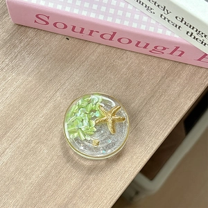 Detail of round ocean style phone grip with gold starfish and green stones on wood