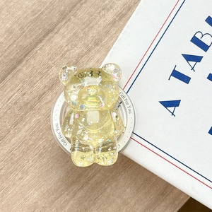 Macro shot of yellow glittery bear phone grip with sequins on light wood desk