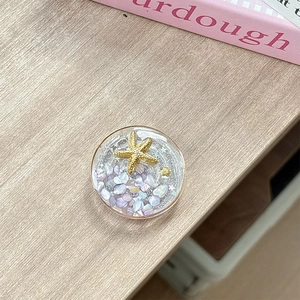 Detail of a round resin phone grip featuring a golden starfish and purple stones