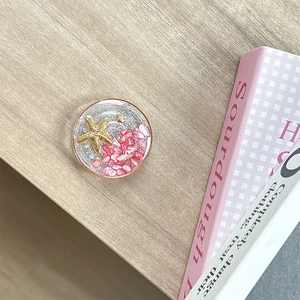 Detail of magnetic phone grip featuring sea stars and pink stones on wooden background