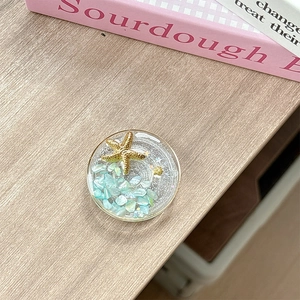 Close-up of ocean-themed phone griptok with shells and gold stars in resin