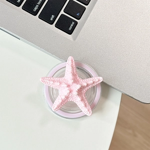 Top view of a pink 3D starfish phone grip stand on a desk next to a laptop