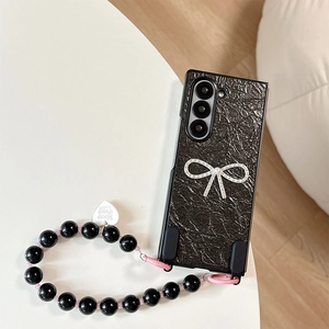 Dettaglio custodia pieghevole in pelle nera con fiocco strass e cinturino in perline