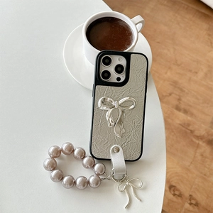 Detail of silver crinkled leather iPhone case with pearl bow strap on a coffee table