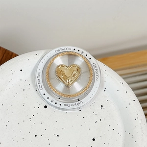 Close-up of golden heart phone grip with Gift For You text and clear acrylic ring detail