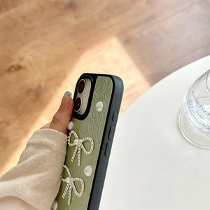 Detail of light green leather-textured phone case with pearl and rhinestone bows
