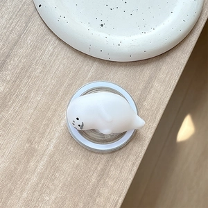 Close-up of a white seal squishy phone grip on a minimalist light wood background