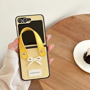 Detail of yellow leather fold phone case with 3D white bow and integrated hand strap