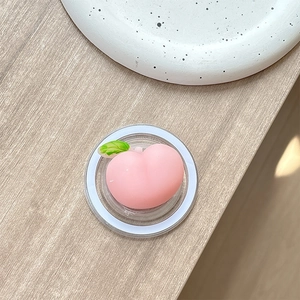 Detailed view of a soft pink peach phone grip with green leaf detail on a wooden desk