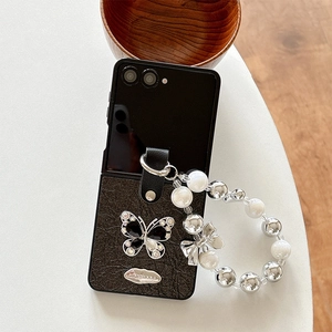 Detail of stone-textured leather phone case with rhinestone butterfly and beaded handle