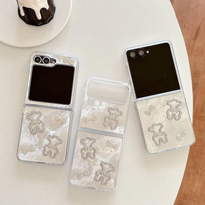 White pearl Z Flip 6 case with rhinestone bear and bowknot on a minimalist table