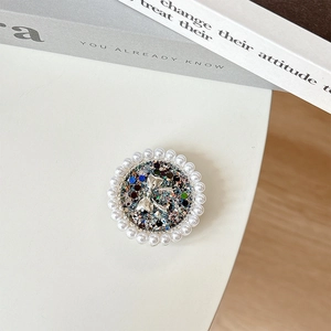 Detail of round phone grip with glitter base, silver bowtie and pearl rim on white desk