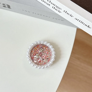 Detail view of round pearl phone grip with a glittery silver bow tie and sequins
