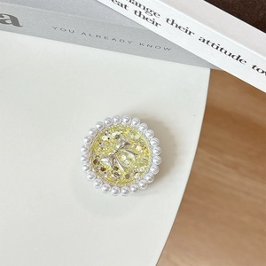 Detail of round phone grip with yellow glitter base, silver bow, and pearl border