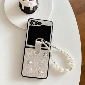 Macro shot of silver textured folding phone case with butterfly charm and pearl wrist strap