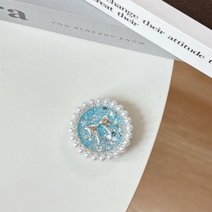 Detail of round pearl phone grip with blue glitter and silver bow on white desk