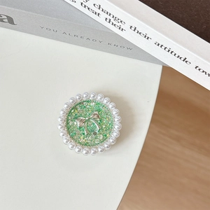 Detail view of round green glitter phone grip with silver bow and pearl decoration