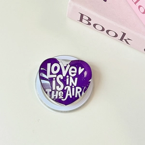 Nahaufnahme einer lila herzförmigen Handyhalterung mit der Aufschrift LOVE IS IN THE AIR