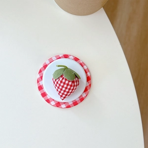 Detailed top view of a fabric strawberry emblem on red gingham circular base