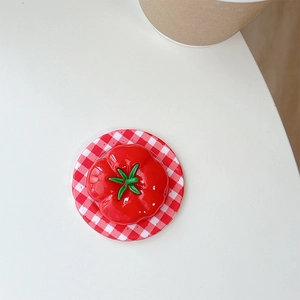 Close-up of a creative 3D tomato-shaped phone grip with green stem on a red checkered base