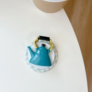 Macro top view of miniature teal teapot phone grip with golden handle on a tray
