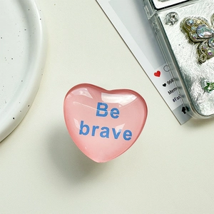 Makro-Detail des herzförmigen Handy-Griffs mit Be Brave Text auf weißem Tisch