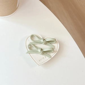 Détail de nœuds en ruban vert sur support cœur en cuir blanc avec texte gaufré