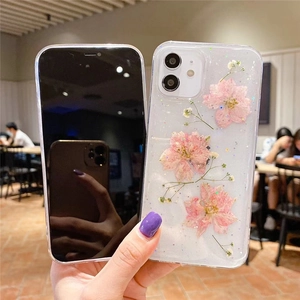 Coque iPhone transparente avec fleurs roses séchées et paillettes tenue par un mannequin