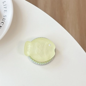 Close-up of cute yellow fish phone grip with green pearl base on a white surface