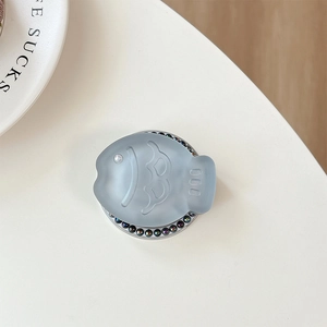 Close-up of light blue fish phone grip with colorful rhinestones on a beige table