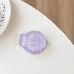 Macro detail of purple fish-shaped phone grip with glitter and pearl accents on white desk