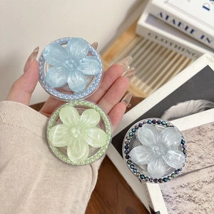 Three translucent glitter flower phone grips with pearl accents on a wooden background